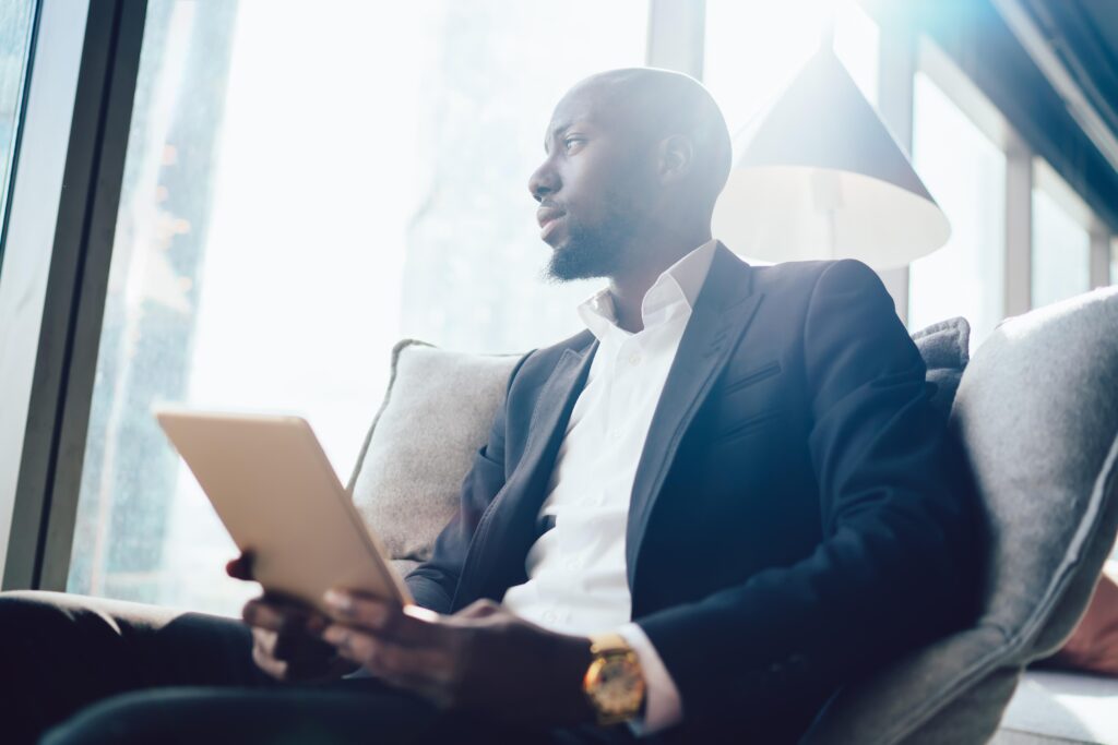 Pensive black businessman with tablet in sunlight